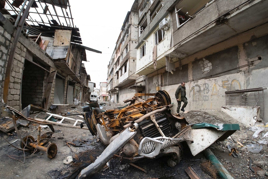 A man walks in the yard of an apartment building damaged by shelling and strown with rubbish.