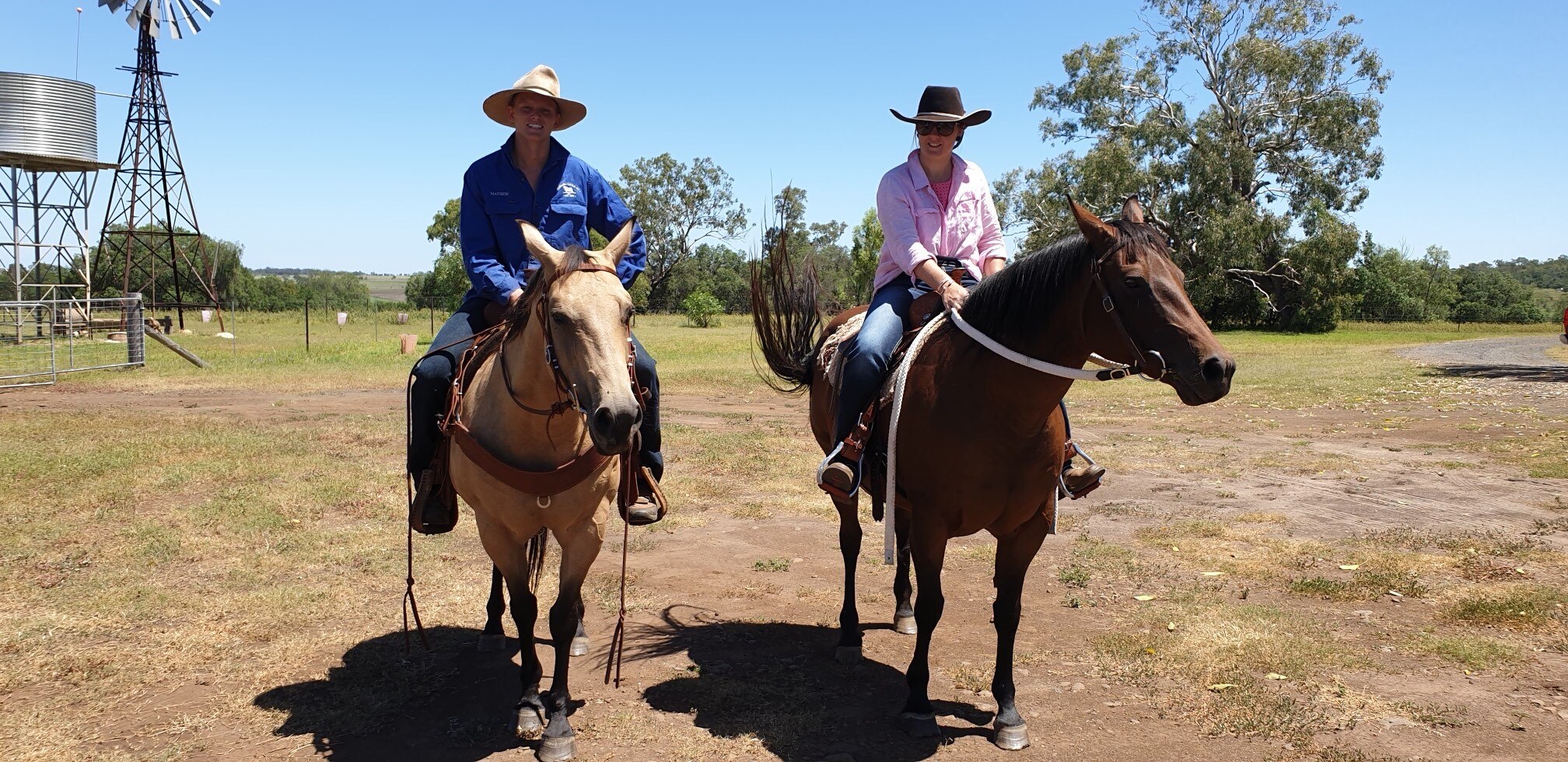 Young couple on a pair of horses in the hot sun with windmill in the distance.