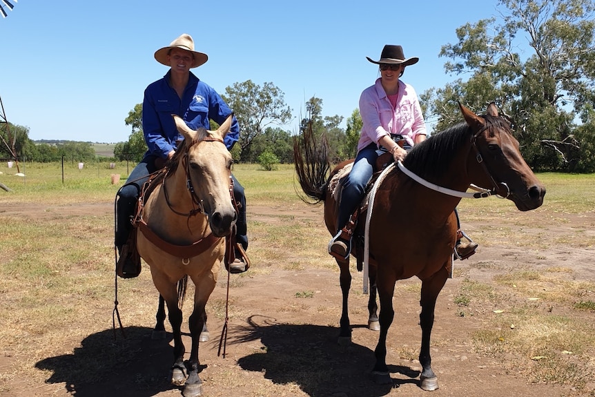 Young couple on a pair of horses in the hot sun with windmill in the distance.