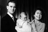 Prince Philip cradles a baby Prince Charles, with Queen Elizabeth II playing with his hand.