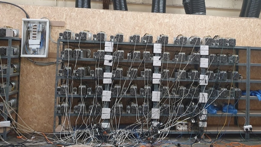 Dozens of computer units sit on shelves among power cables