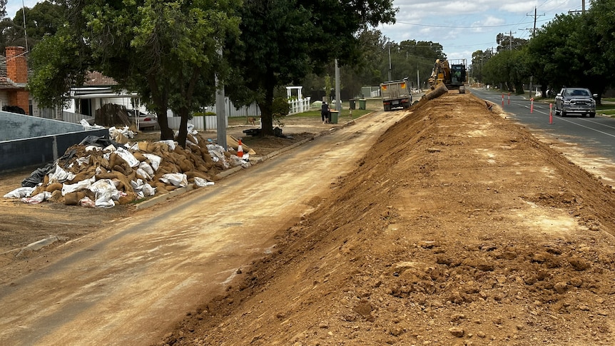 A levee made of dirt runs along a suburban street.