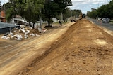 A levee made of dirt runs along a suburban street.