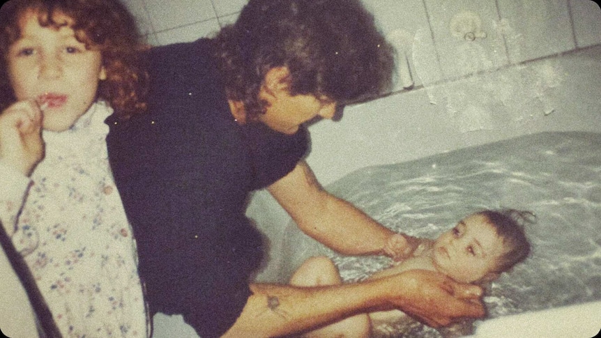 An old, grainy photo showing a man bathing one baby girl and another older girl brushing her teeth.