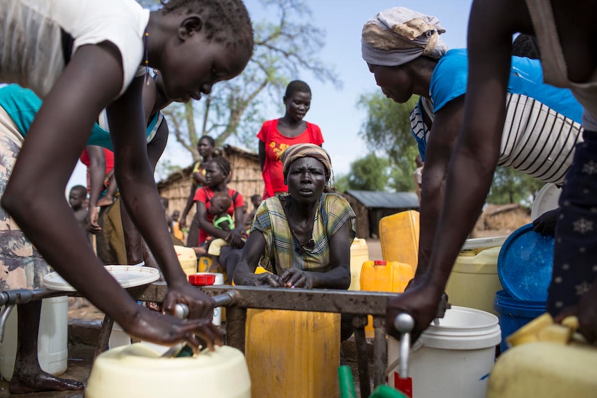 Refugees from Sudan carry plastic bottles as they gather to collect water from a water point.