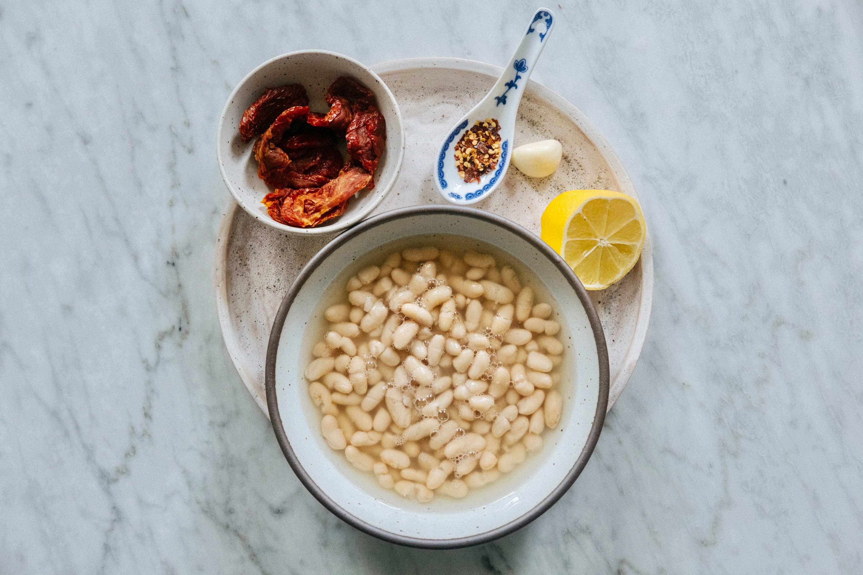 An aerial view of ingredients for a dip, inclduing tinner beans, sun-dried tomatoes and spices.