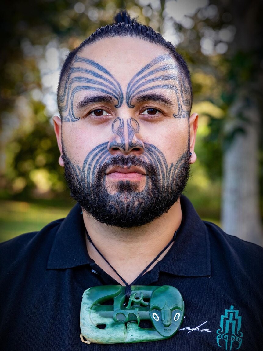 Une photo de profil serrée d'un homme aux traits sombres et aux tatouages ​​faciaux maoris sur le front, les joues et le nez 