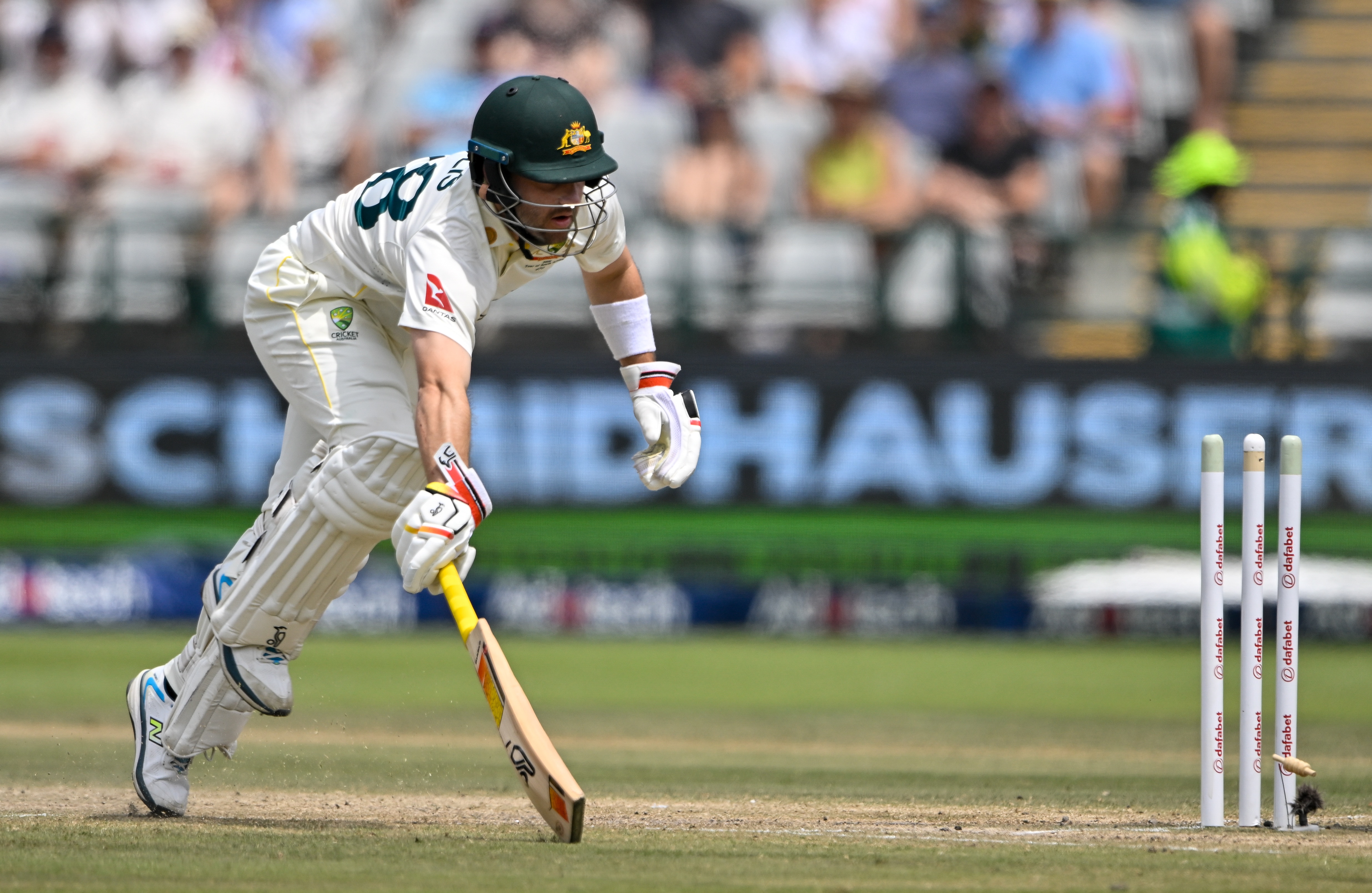A cricket batter struggles to down his bat in time as the stumps are broken