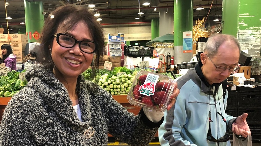 A woman with dark hair and glasses holding up a strawberry punnet and smiling.