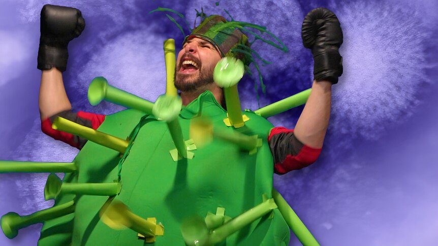 Joe dressed up as a virus and wearing boxing gloves throws his hands up in celebration.