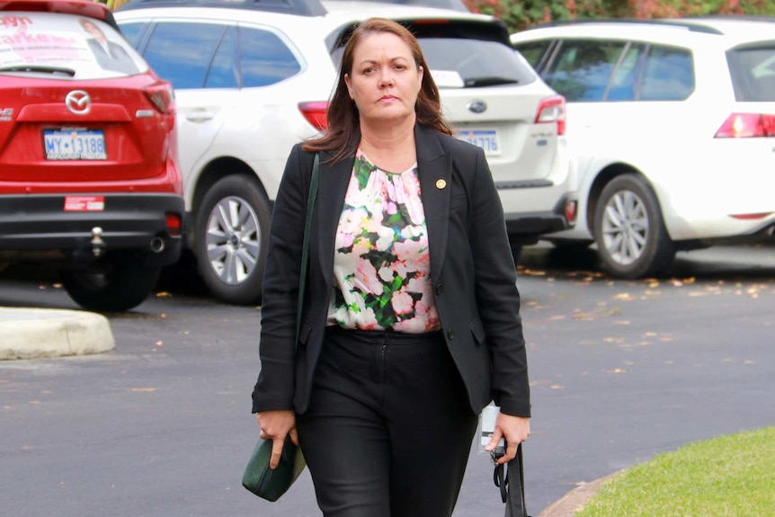 A mid-shot of Liza Harvey walking towards the camera from a carpark.