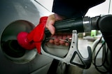 A hand holds the bowser pumping petrol into a car