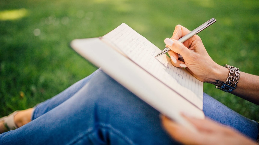 Close-up of woman writing a note in the grass for a story about writing letter to have tough conversations with your partner.