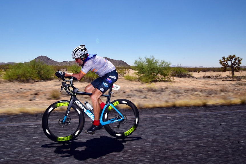 Cyclist Allan Jefferson rides on a road with mountains in the background