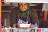 Iraqi refugee Fadhaa Al-Khalidi leans out of the window of her Fare Go food truck holding a tray and smiling.