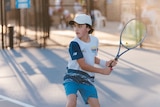 An Aboriginal teenager holding a racquet about to hit a tennis ball.