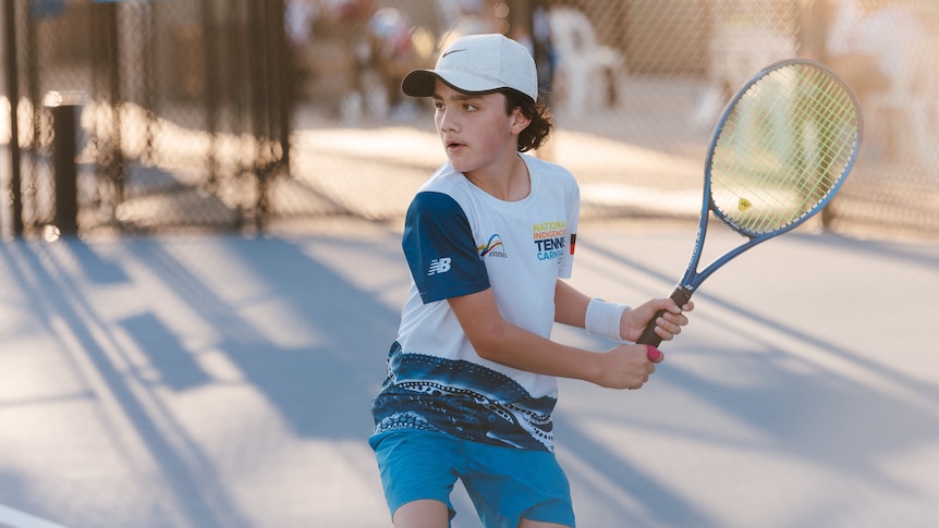 An Aboriginal teenager holding a racquet about to hit a tennis ball.
