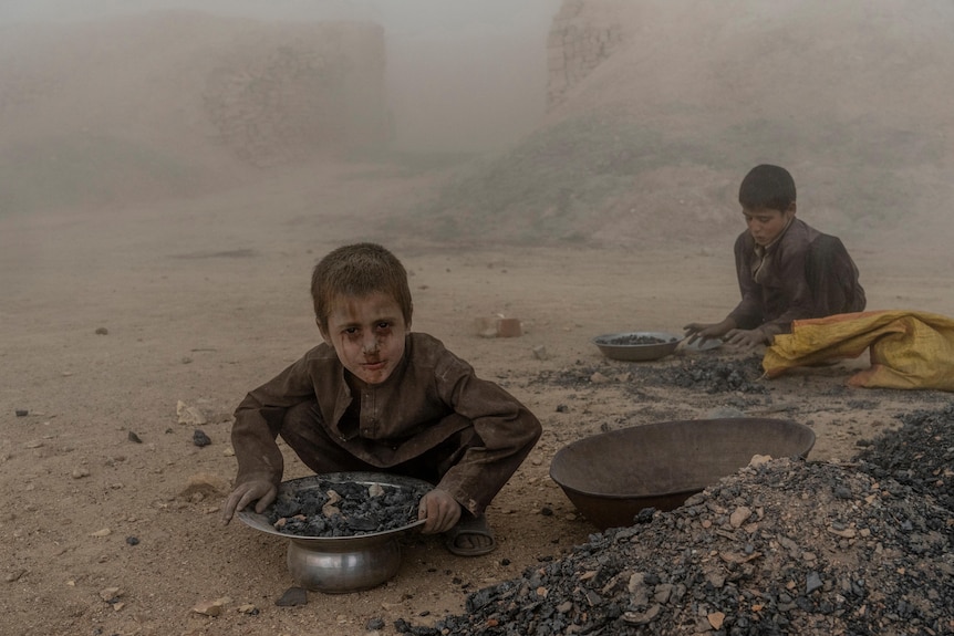 two boys file pans with debris with their faces covered in dust