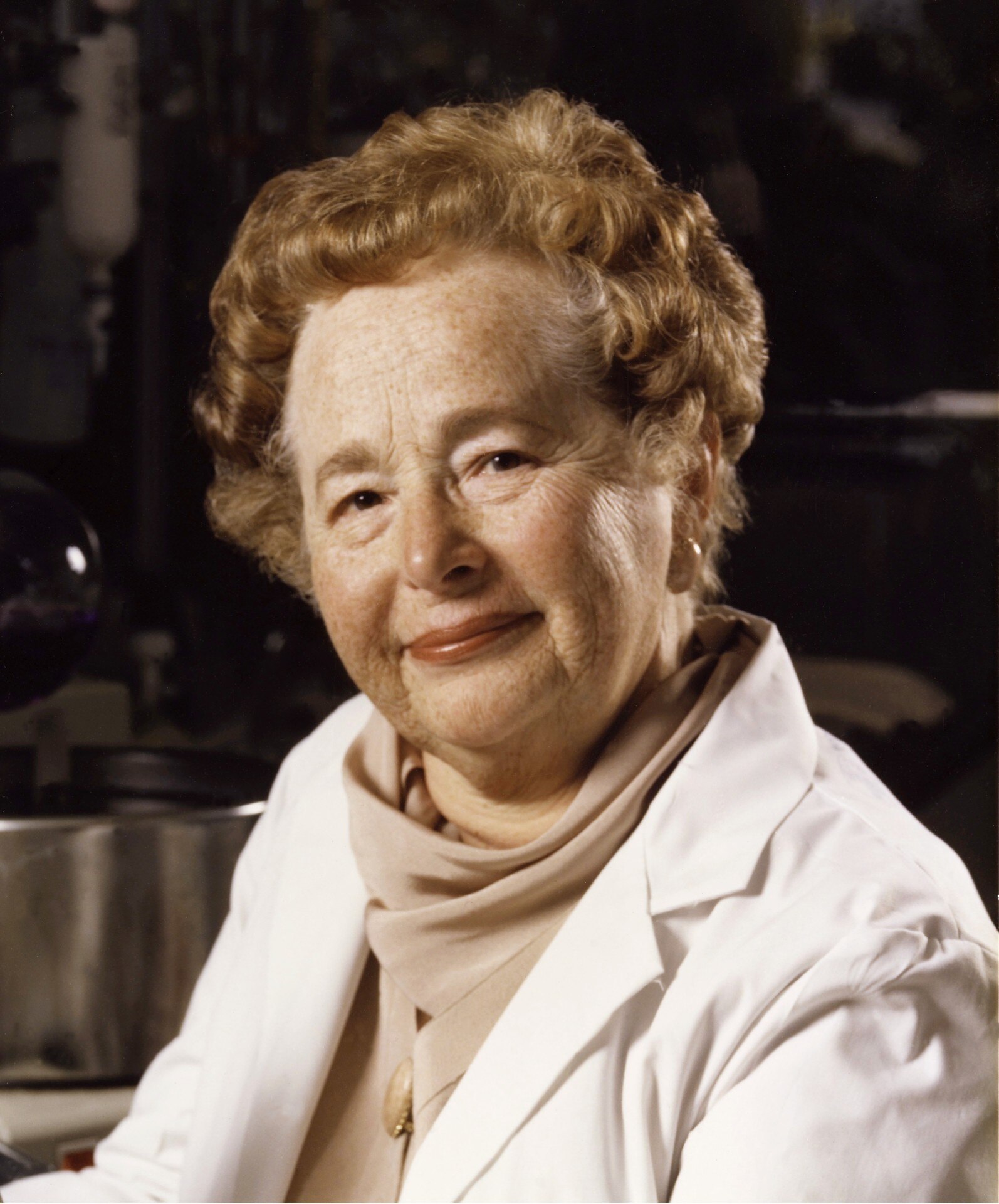 An older woman with short permed hair and white lab coat