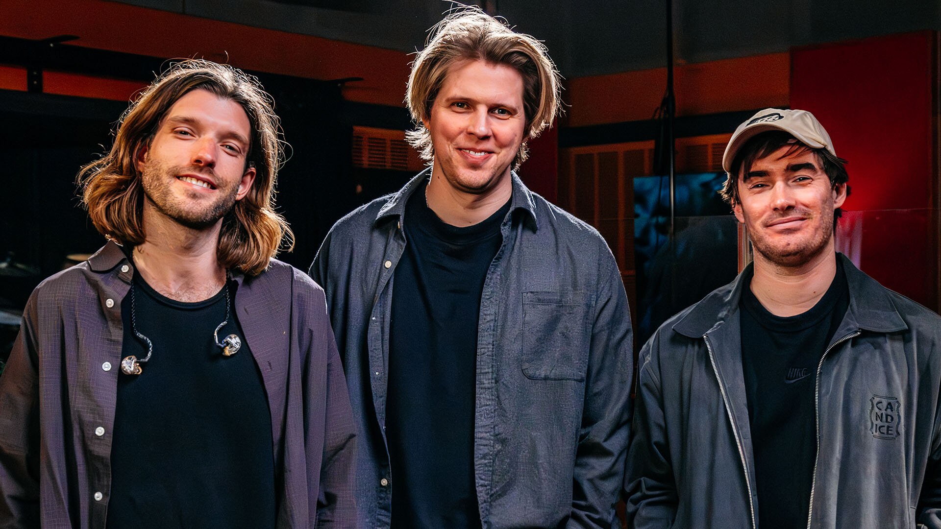 Three men smile towards the camera, wearing navy shirts or jackets over black t-shirts.
