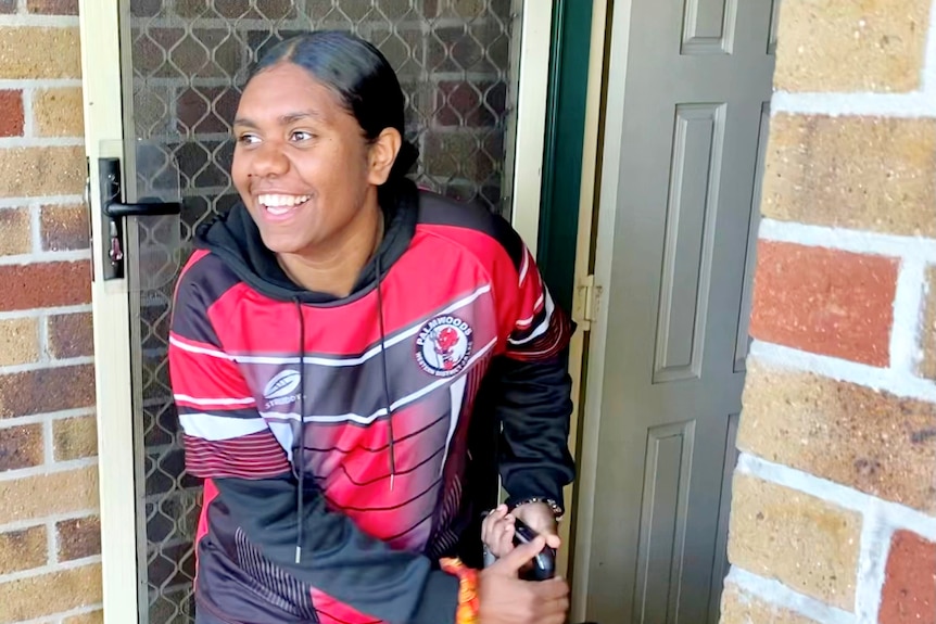 Young woman with a suitcase coming out the door, smiling