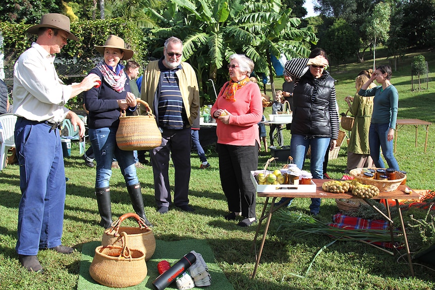 A group of people standing around blankets and tables filled with home-grown produce, jars of preserves and egg cartons.