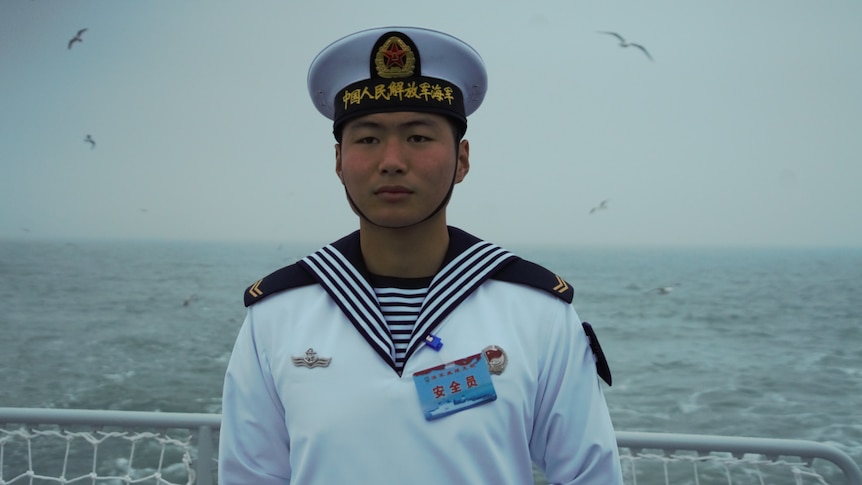 A Chinese sailor stands at a railing on a ship