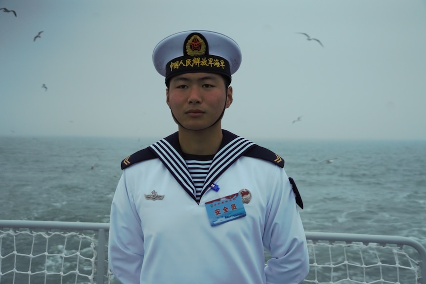 A Chinese sailor stands at a railing on a ship