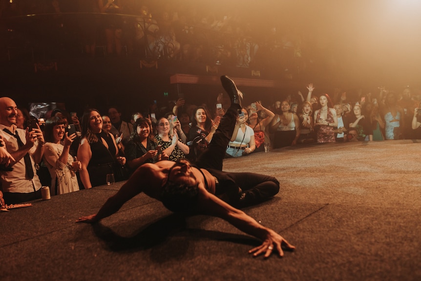 A man lays on the stage, his leg thrust in the the air. 