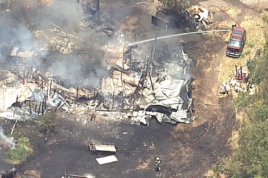 Twisted metal and burnt wood remain from a destroyed home, a firefighter shoots water at the scene.