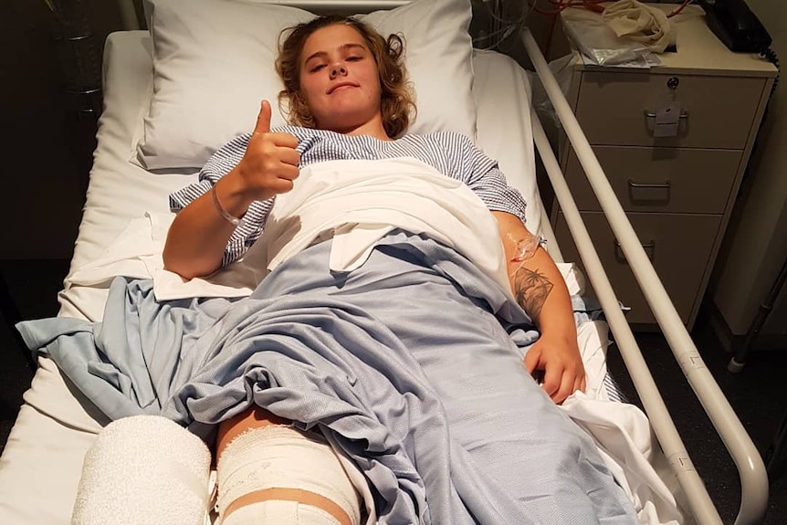 Injured footballer Chloe Scheer gives a thumbs up while laying in a hospital bed