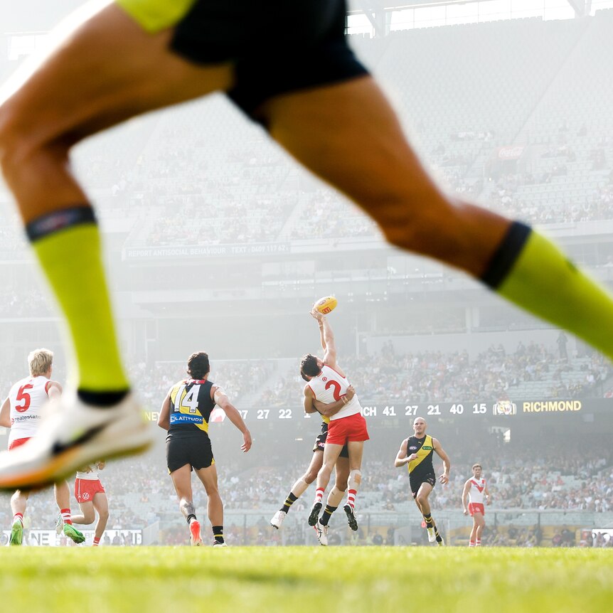 A photo taken through the umpire's legs across the ground as Tigers and Swans play in a haze.