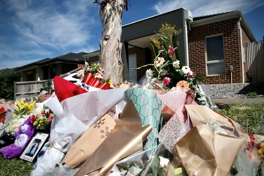 Floral tributes lay by a tree in front of a suburban house.