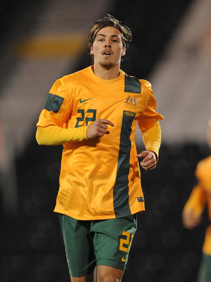 A male soccer player wearing yellow and green runs towards the camera