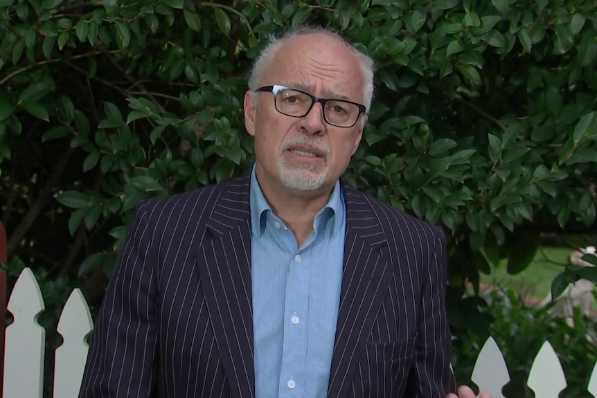 A man with glasses standing in a garden setting.