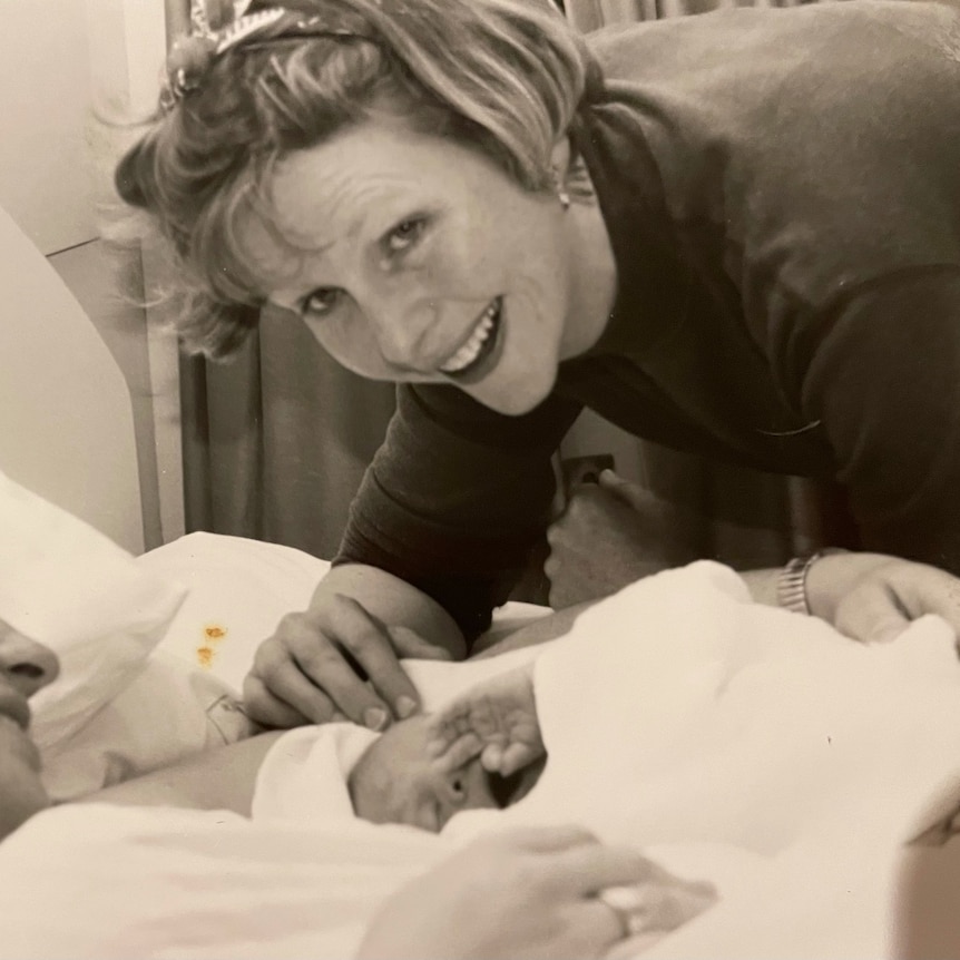 An old black and white photo of Helen Haines leaning down over a mother and newborn baby