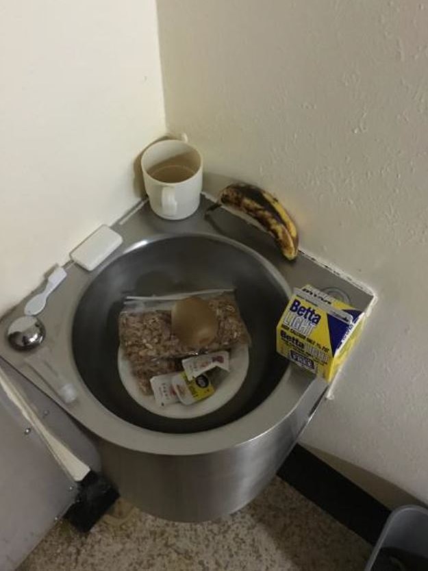 A prison cell toilet being used as a table for a cup, banana, milk carton and other breakfast items.