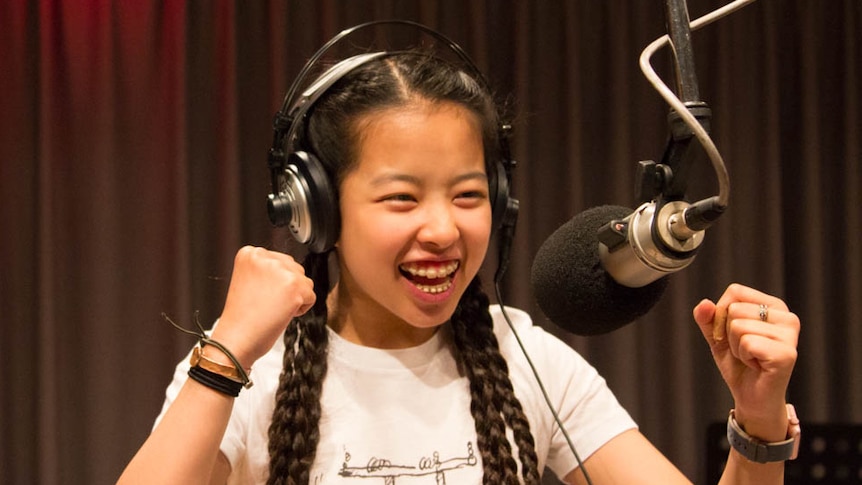 Madison in radio studio wearing headphones and talking into microphone with big smile and fists up.