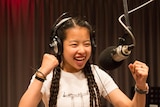 Madison in radio studio wearing headphones and talking into microphone with big smile and fists up.