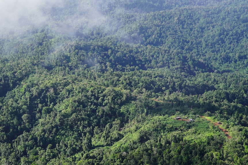 An aerial view shows a green mountainous region with a small outcrop of houses in one corner