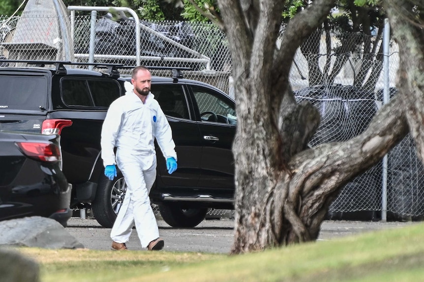 A man in white forensics gear walking from a black car