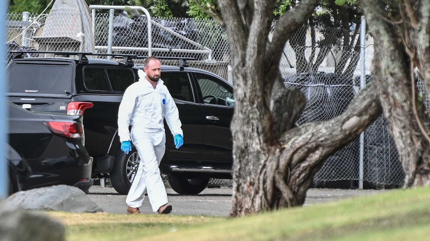 A man in white forensics gear walking from a black car