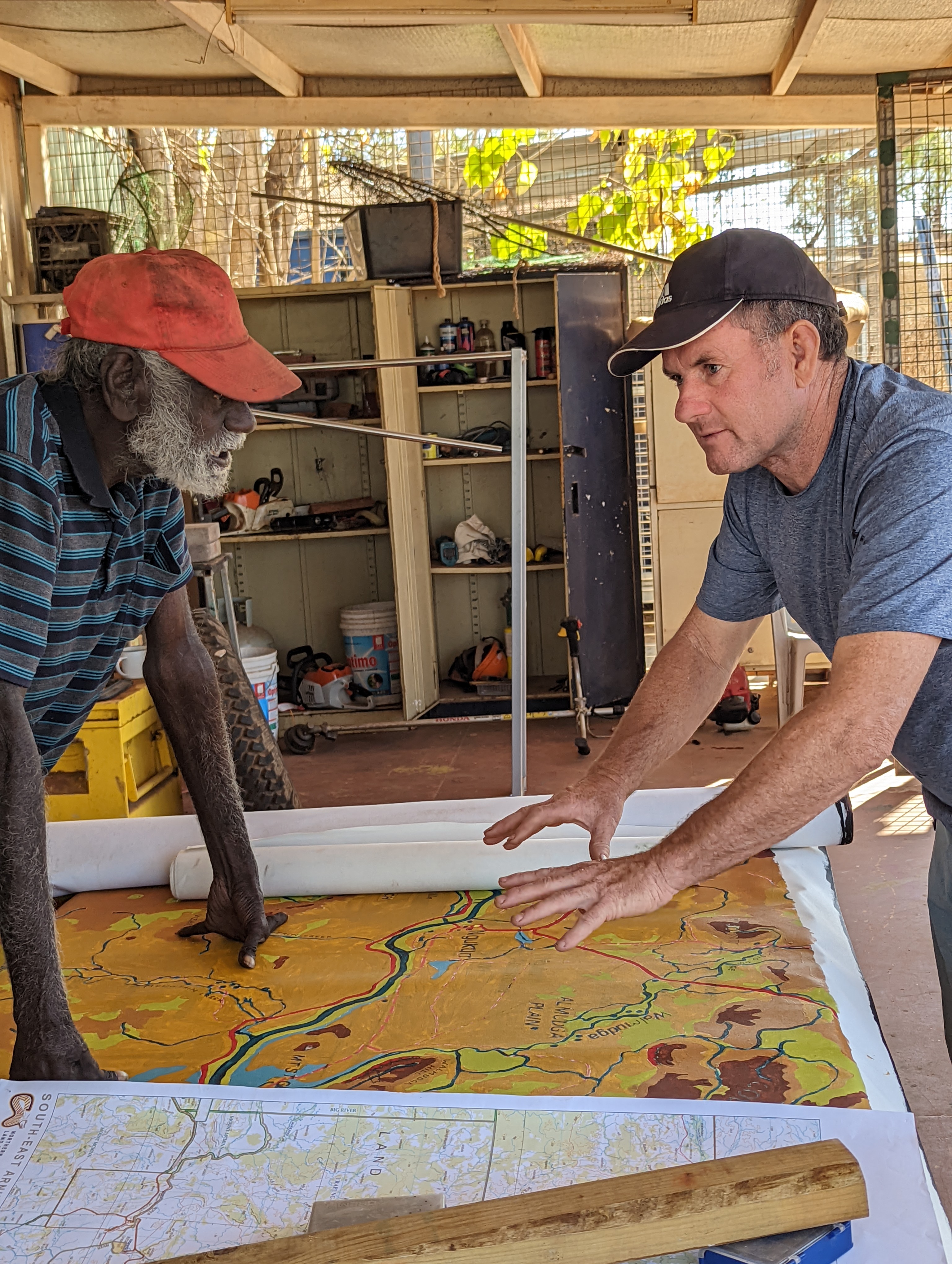 An Indigenous man and a Caucasian man survey a part of the 13-metre long map over a table.