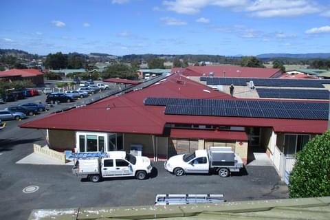 An aerial picture of two white utilities parked in front of a yellow brick building with red roof and solar panels..