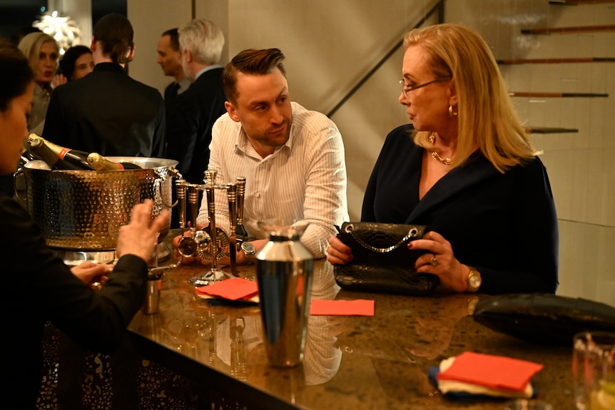 Roman and Gerri talk at the bar of a party.