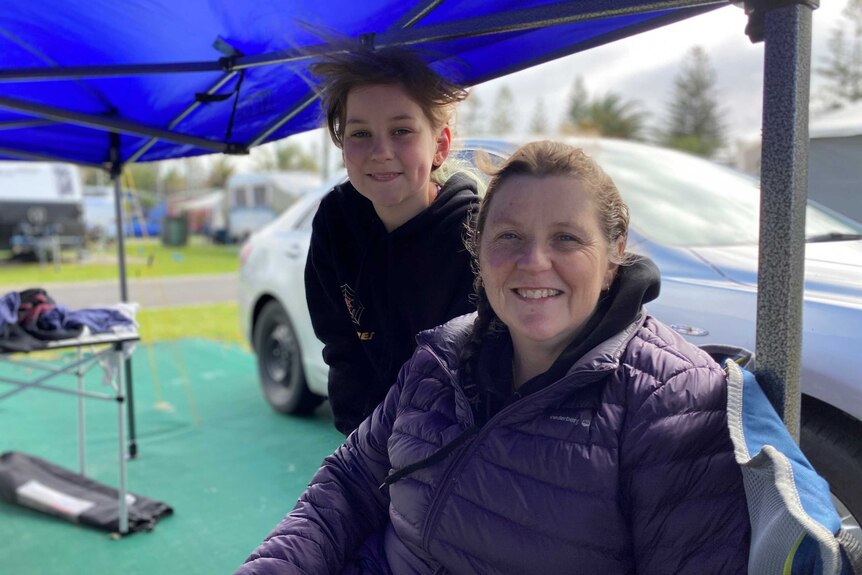 A mother and daughter under a pop up tent smile at the camera.