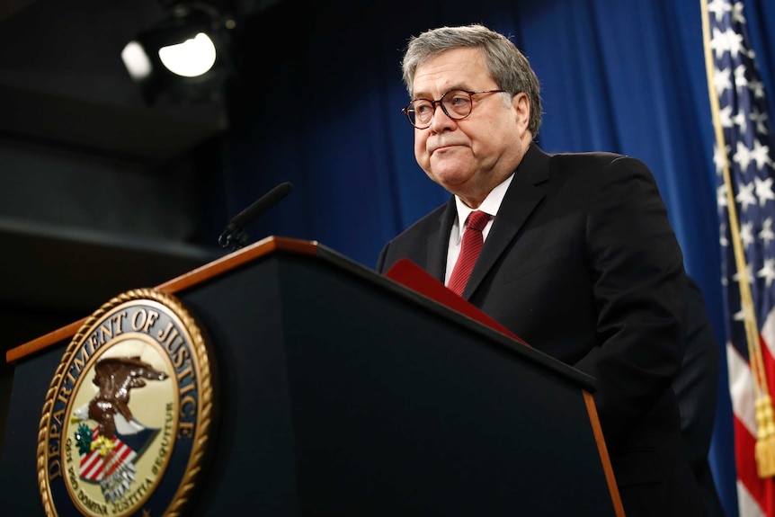 Attorney General William Barr wears glasses and speaks at a podium with the Department of Justice seal.