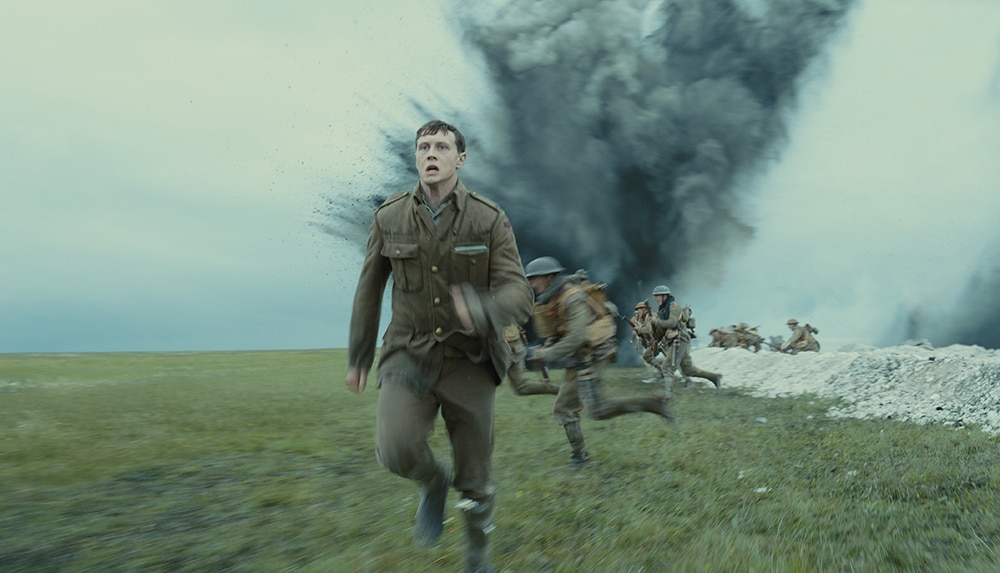 A group of men in world war one brown uniform run at speed from trench near large cloud of smoke and debris.