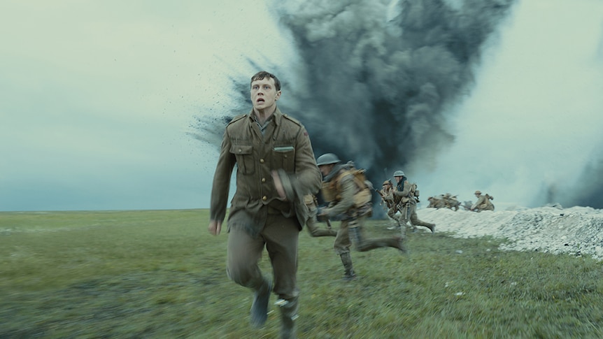A group of men in world war one brown uniform run at speed from trench near large cloud of smoke and debris.