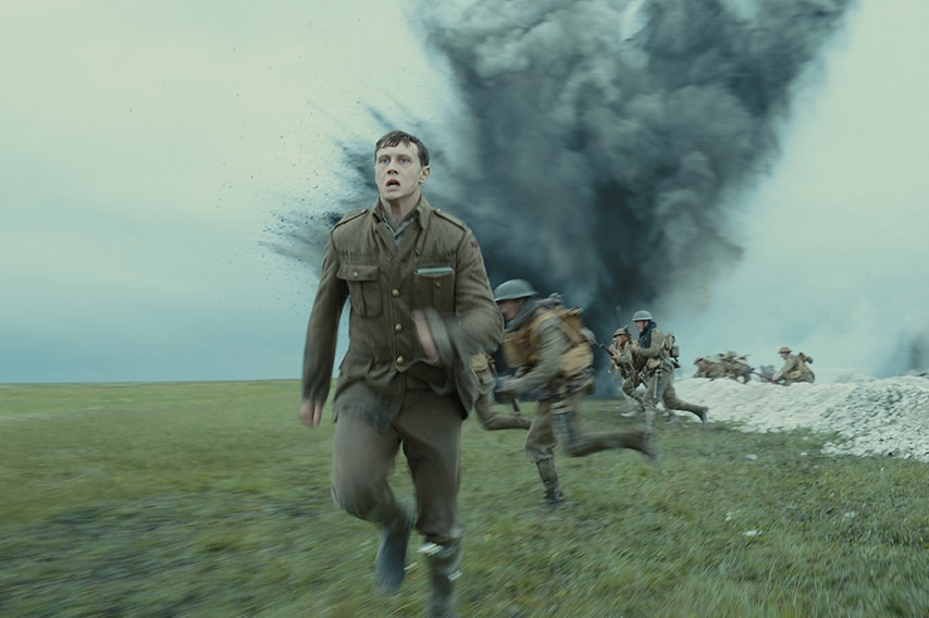 A group of men in world war one brown uniform run at speed from trench near large cloud of smoke and debris.